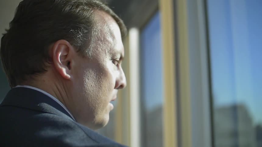 A man in a business suit is staring out the window of a high-rise