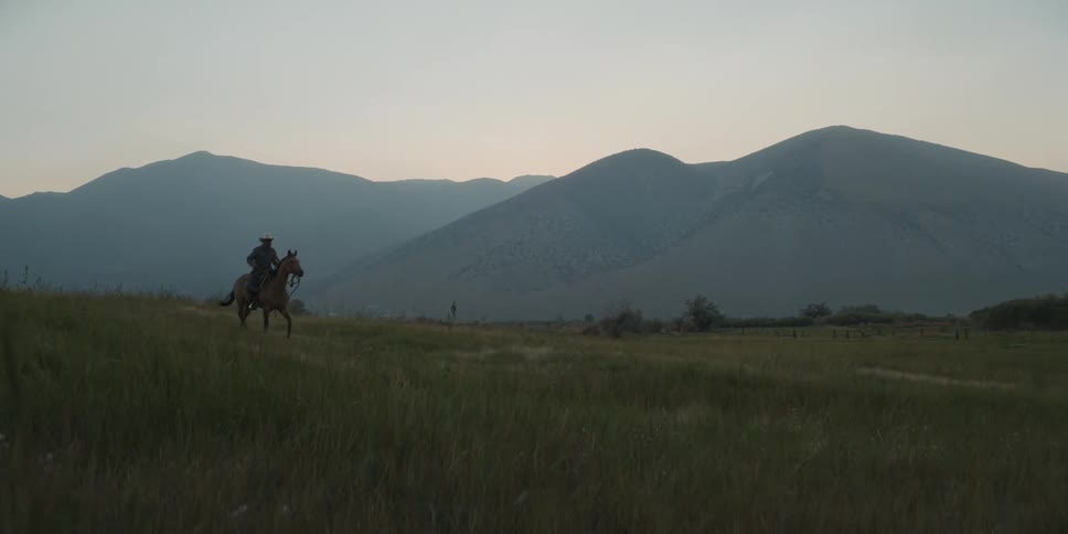 A cowboy rides his horse past the fog covered mountains