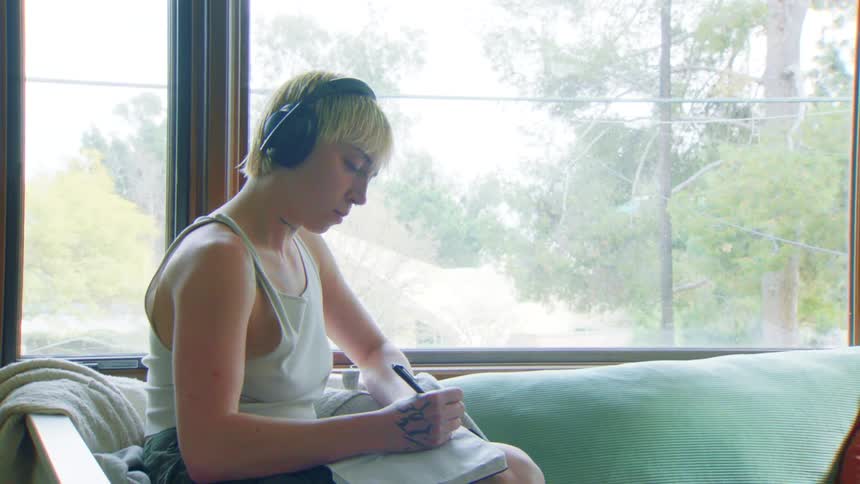 The teenager is listening to music and writing in her notebook
