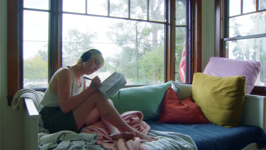A woman listens to music while writing in her notebook