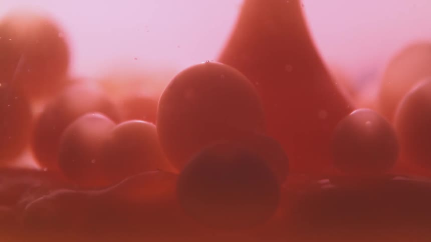 Red drops fall to the bottom of a container of liquid