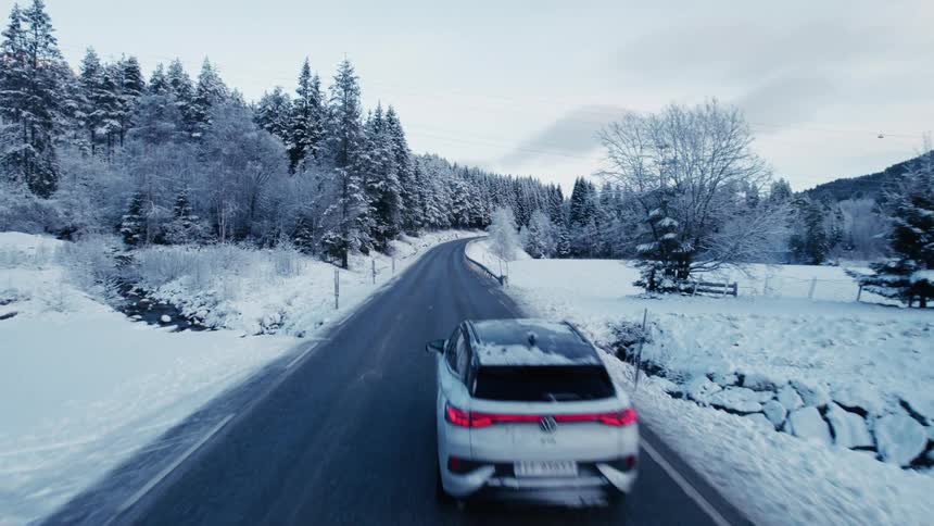 Car drives over a stream and past forested slopes on a rural highway in winter