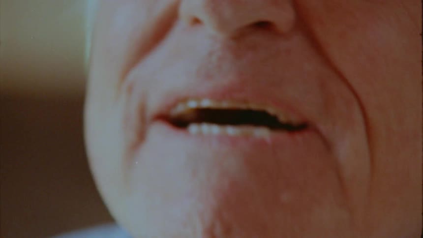 An extreme closeup shows an elderly man talking and smiling with the focus shifting between his eyes and mouth