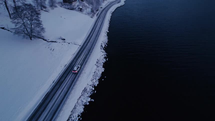 Car traveling along a road by a lake in an environment surrounded by snow
