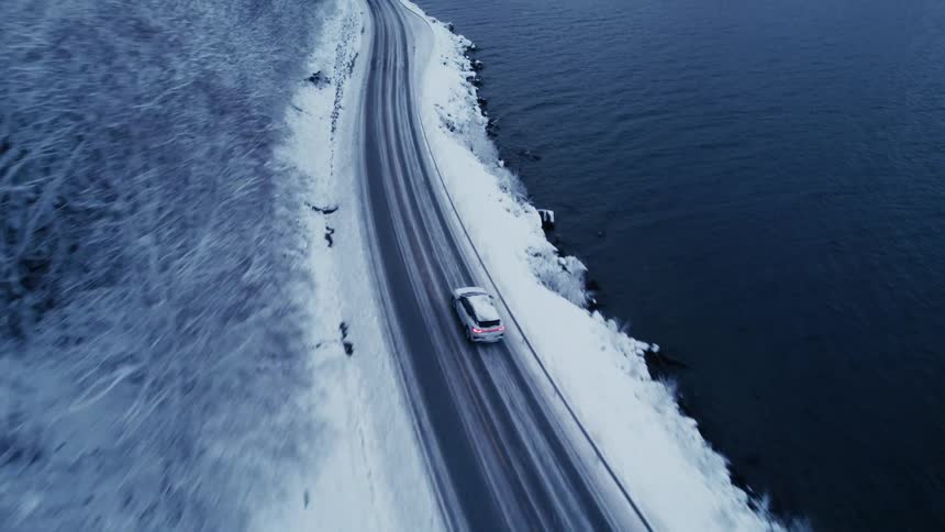 The white car drives on the icy road by the mountains