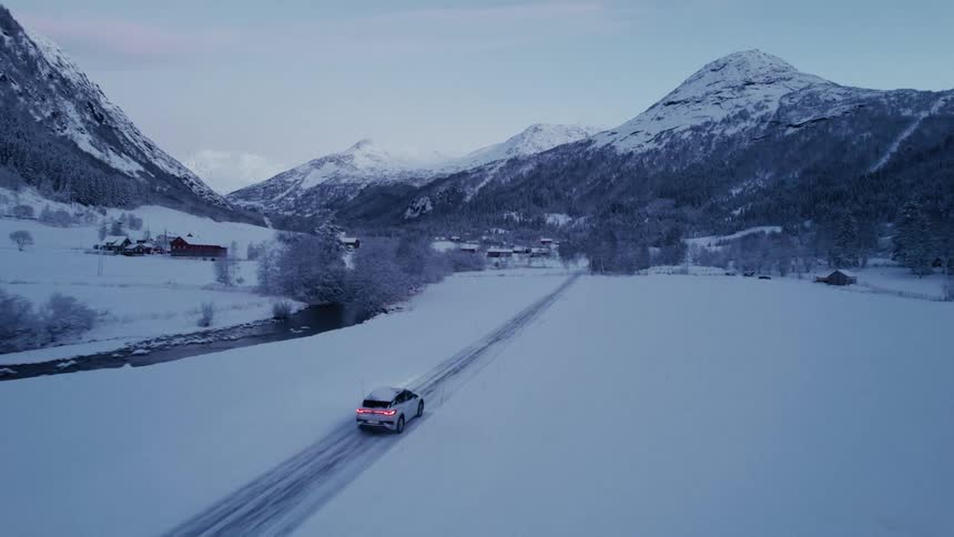 The car drives on the snowy road towards the small town