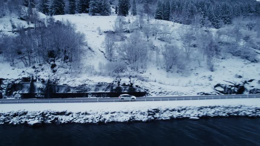 Car traveling on a road by a lake and surrounded by mountains and snowy trees