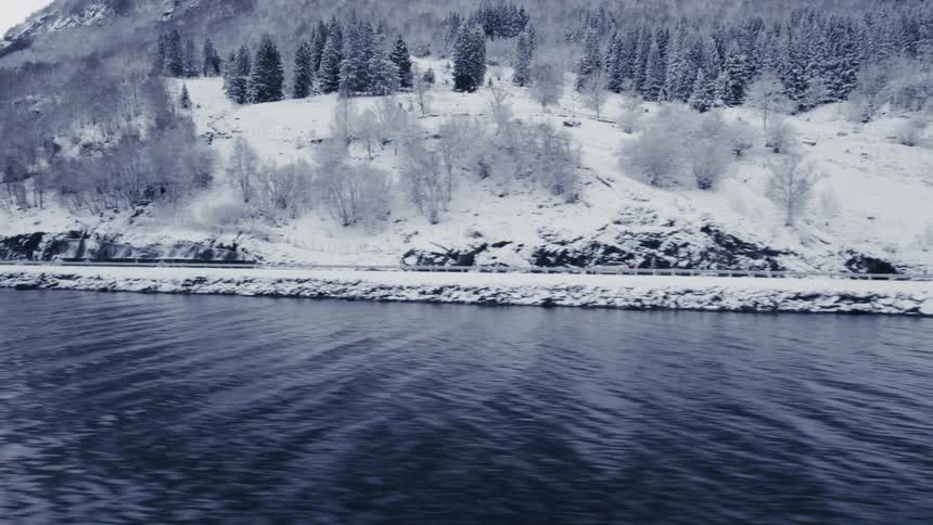 Car traveling on a road by a lake and surrounded by snowy mountains