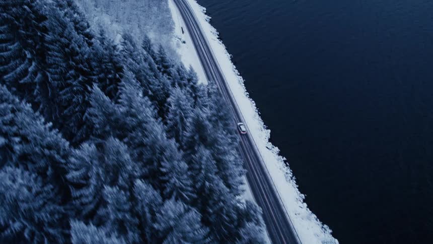 White car traveling along a seaside and coniferous road covered with snow