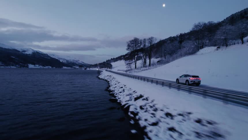 A car driving on an asphalt road next to a large lake with dark water and lots of snow around