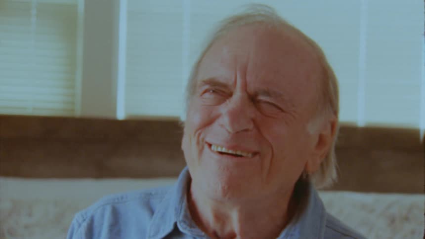 The face of an elderly man who is smiling while talking to someone in front of him