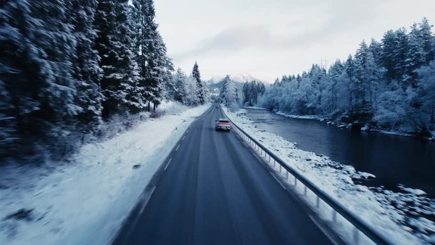 Aerial view of an suv driving on a freeway next to a mountain stream
