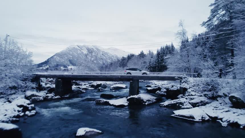 Aerial view of a river bed and a vehicle crossing a bridge over it during winter