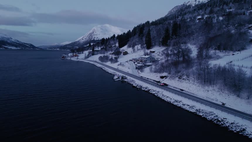 Aerial view of a vehicle passing by village houses in a coastal town by a mountain range
