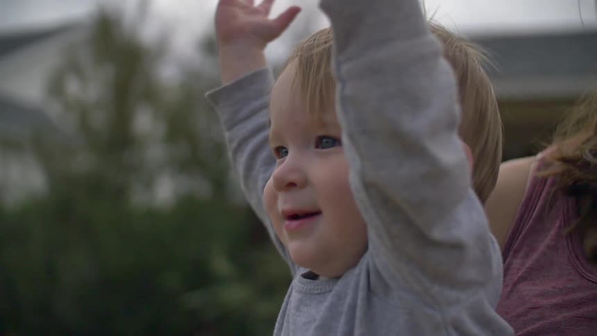 A woman holds a baby lifting his arms into the air