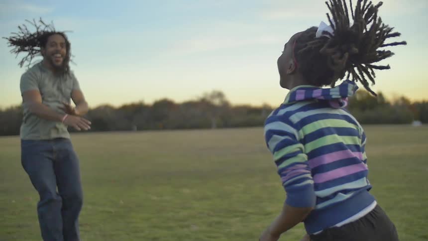A girl and her father are jumping up and down in a field