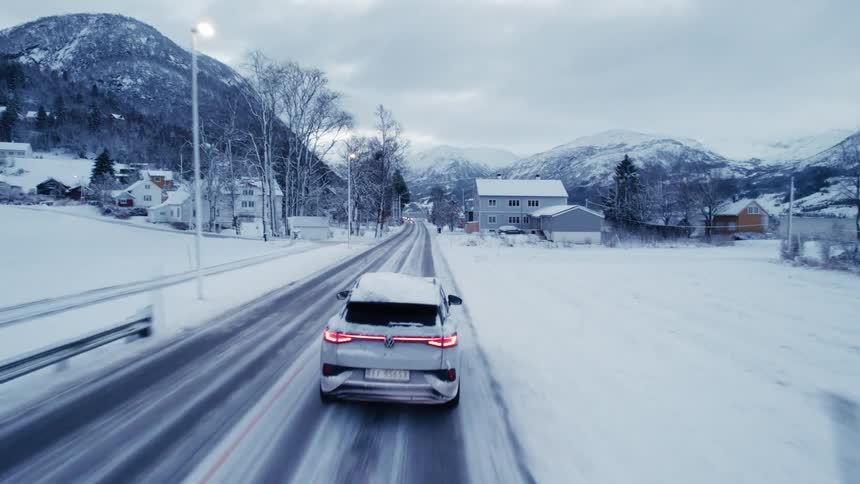 A white car driving on an asphalt road in an environment that is all snowy arriving at a small town