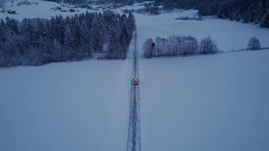 Aerial view of a lone car traveling along a track surrounded by snow and conifers
