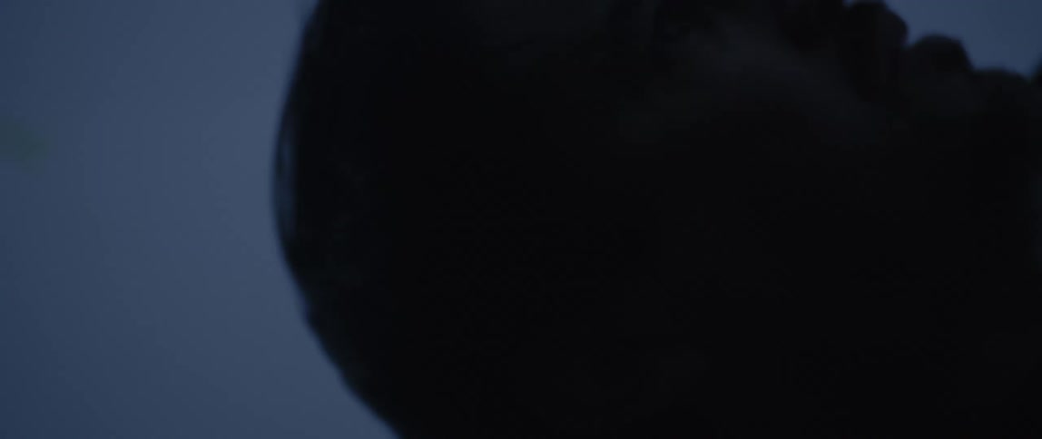A man lies down in a dim bluelit setting as wind gently moves his hair