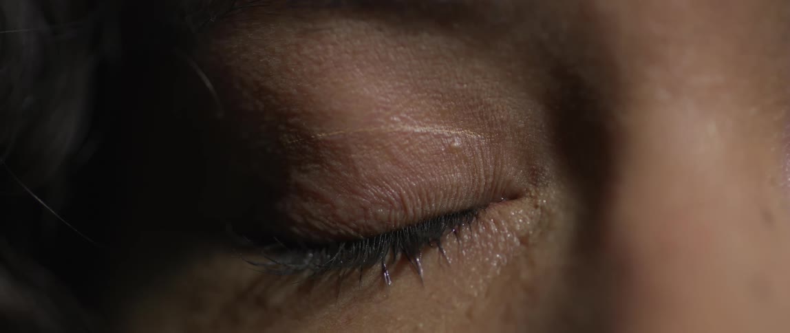 An extreme closeup of an eye slowly opening with visible tears and detailed skin and eyelashes