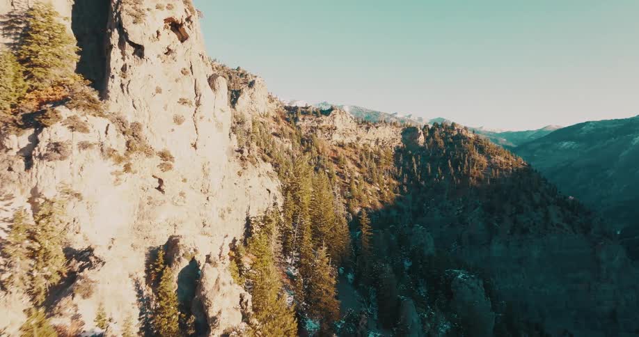 Aerial view of sunlit rugged mountains with steep cliffs and dense evergreen forest