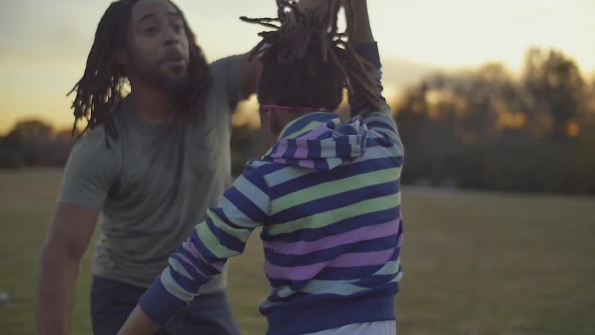 A girl and her father are dancing in a park at dusk
