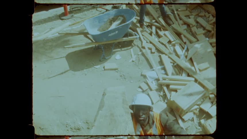 Workers at a construction site manually lift a wooden beam from ground level to the first floor