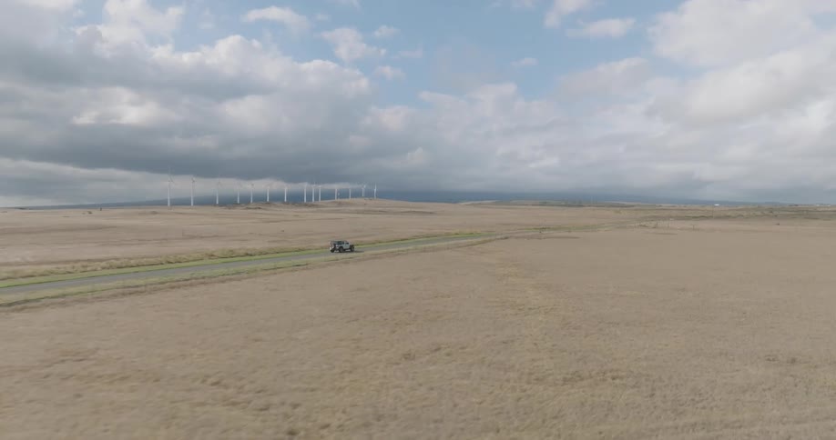 An suv drives on a lonely road surrounded by grass fields on a cloudy day