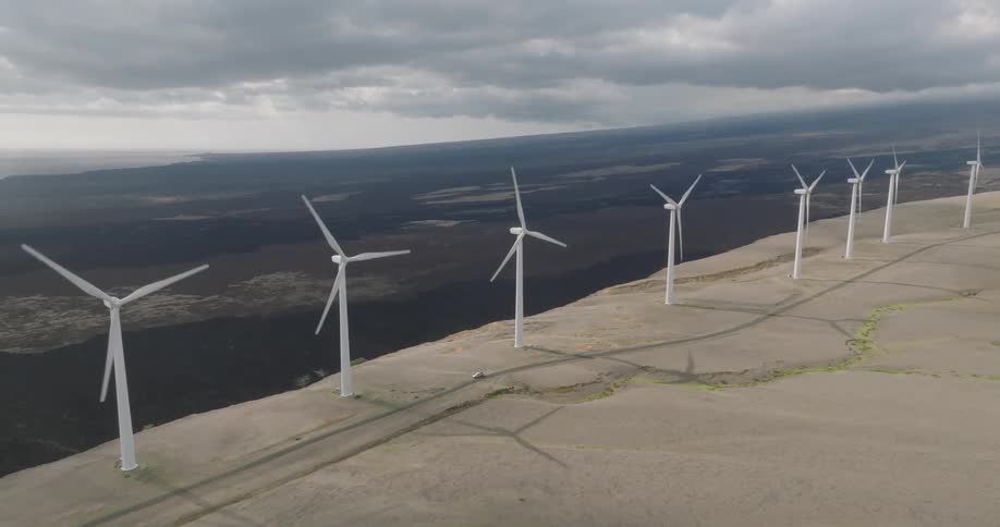 Wind turbines turn slowly on a barren plain casting long shadows in soft overhead light