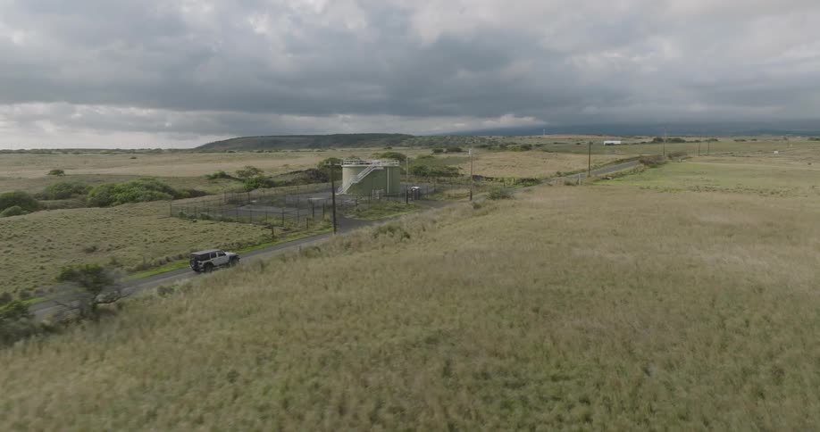 An suv drives on a freeway with grassland on both sides and utility poles lining the side of the road on a cloudy day