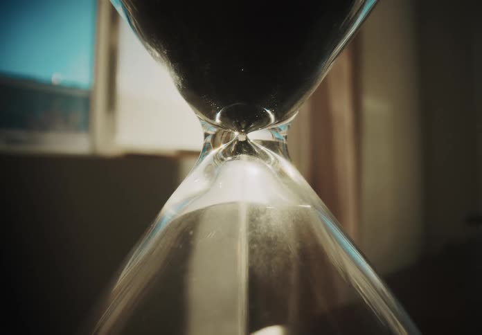 Black sand flows through an hourglass lit by warm sunlight