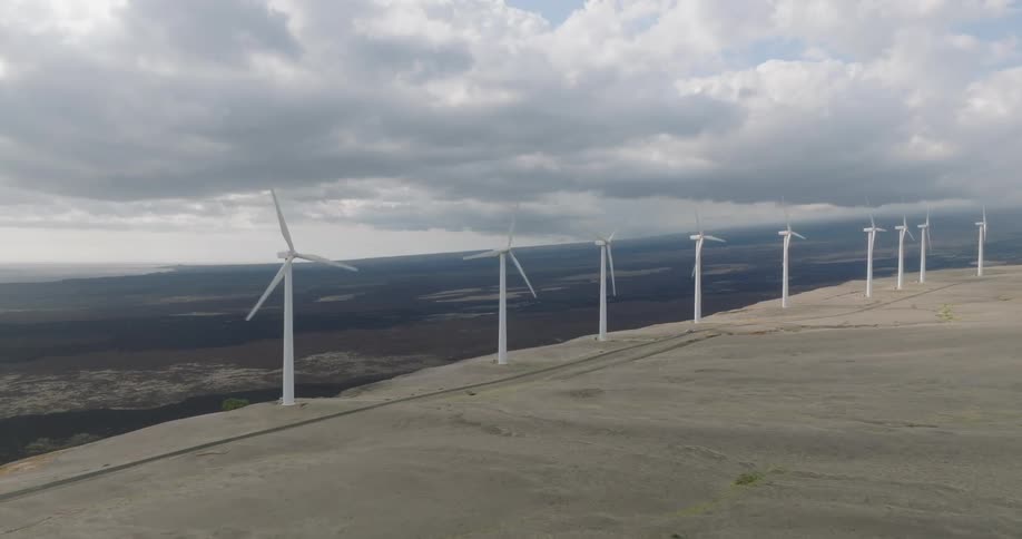 An aerial shot of wind turbines lined across a barren landscape under a cloudy sky