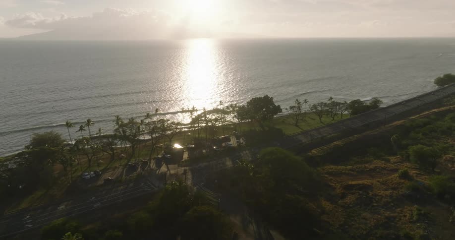 Sun sets over the sea reflecting on the water as a coastal road passes through tropical trees