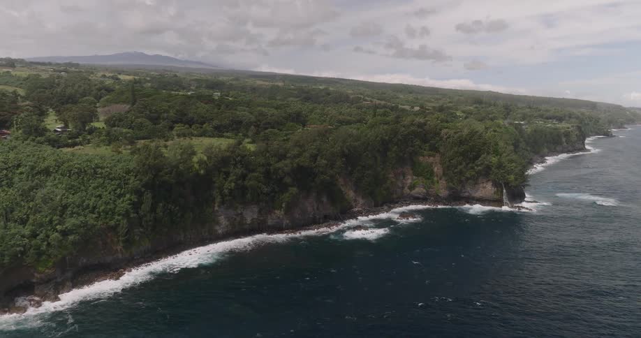 Aerial of ocean waves rolling into a steep shoreline on a mostly cloudy day