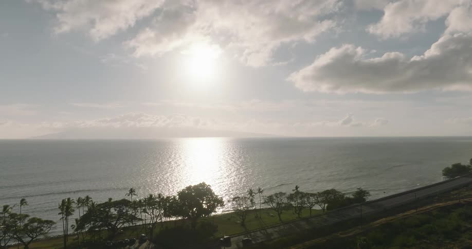 Sun among clouds over the sea with a road cars and trees along the coast