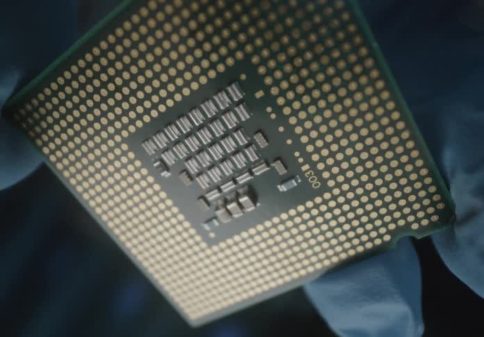 A gloved hand rotates a computer chip revealing its metallic connectors and design