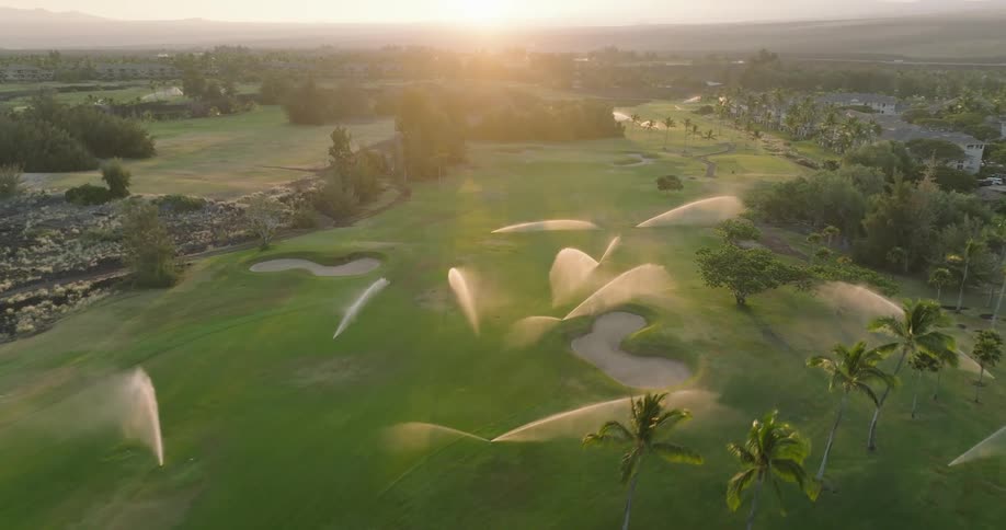 An aerial view of a flat grass field with a few trees and several irrigation points