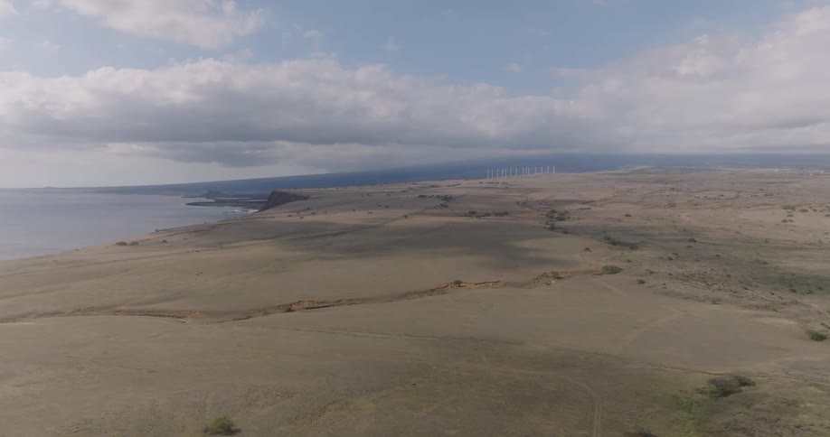 An aerial view of a desert region near a sea on a clear day with white clouds in the sky