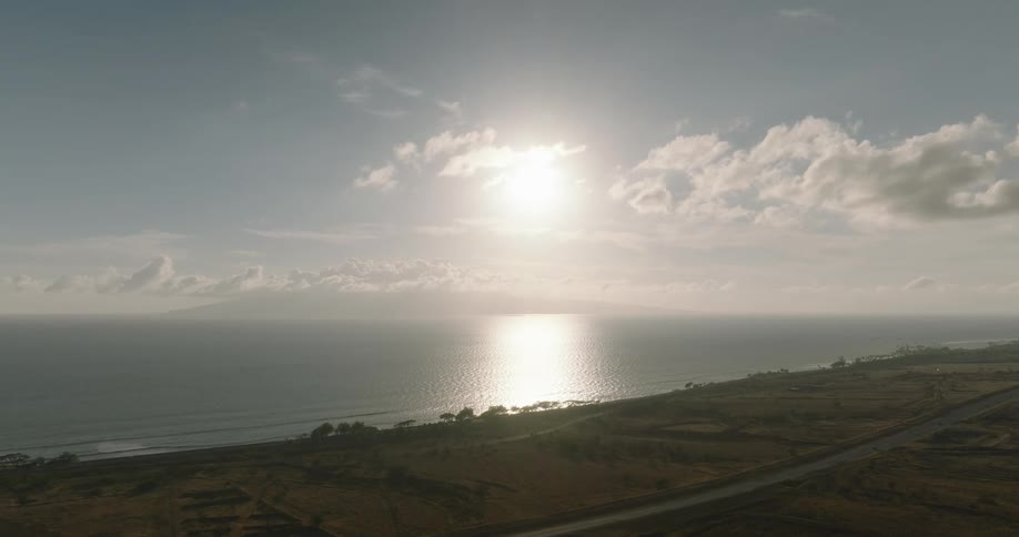 Strip of water stretching from the horizon to the coast reflects the bright sun near a coastal highway