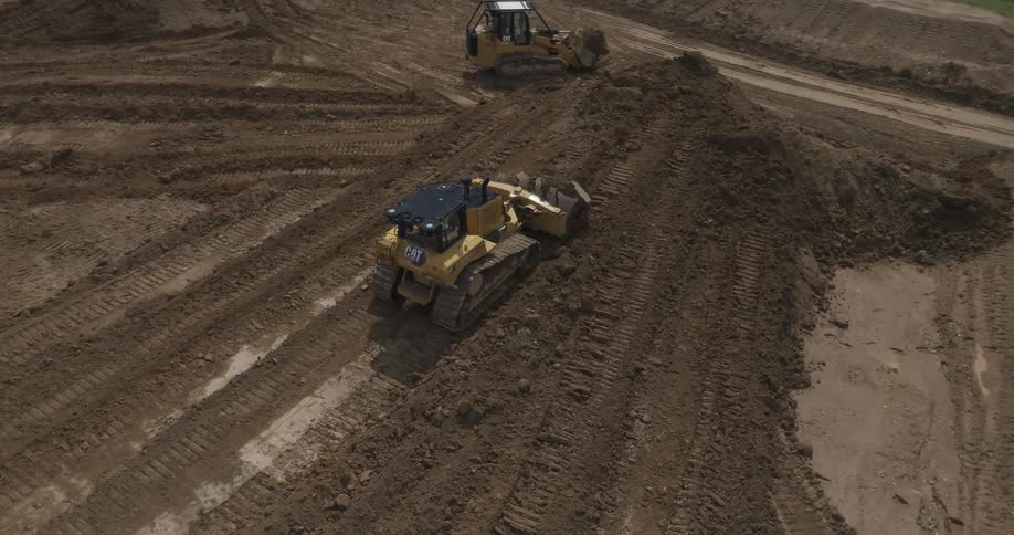 The bulldozer is pushing the dirt on the lot