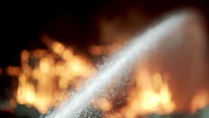 A stream of water is being sprayed onto intense flames likely from a fire hose as part of firefighting efforts