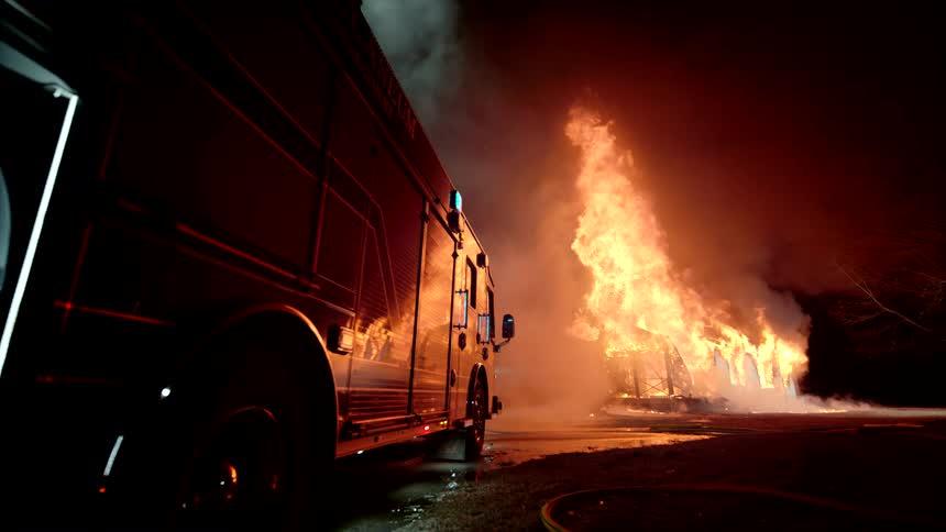 Firetruck parked in front of trees engulfed in flames in at night