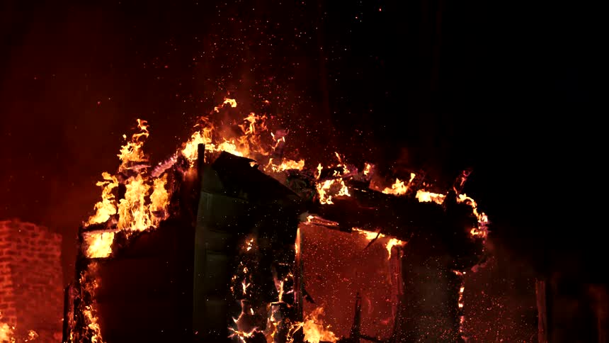 A building is engulfed in flames at night with fire and embers violently consuming the structure