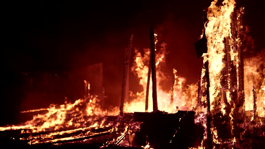 Remainder of a structure burning at night in slow motion