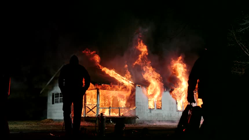 Firefighters carry equipment away from the burning home