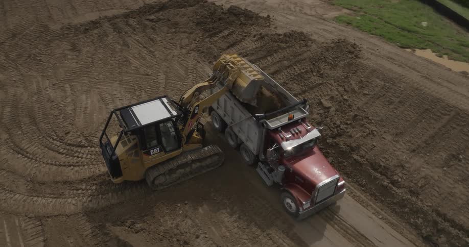 An excavator operator fills a truck with soil on a construction site
