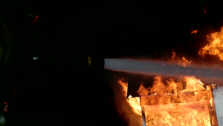 The firefighter is battling a house fire with water from a hose