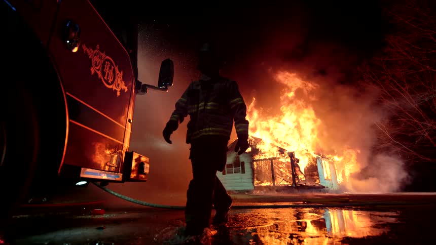 Fireman silhouette walking to firetruck as house rages in flames in background