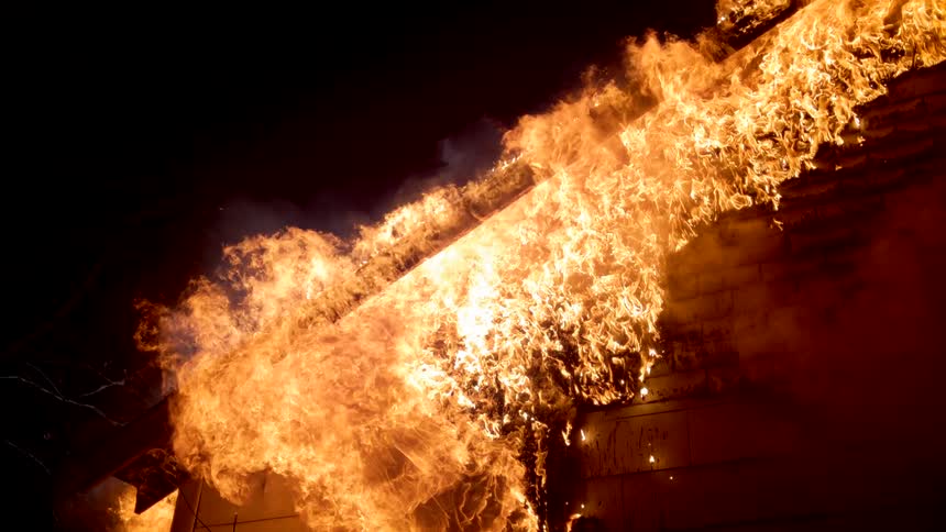 Rooftop of a home engulfed in flames at night