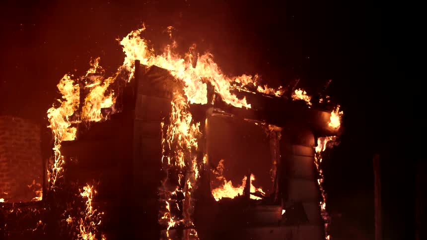Flames engulf the skeletal remains of a structure against a dark night